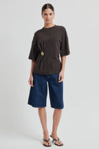 Woman wearing a brown top and blue denim shorts on a light gray background
