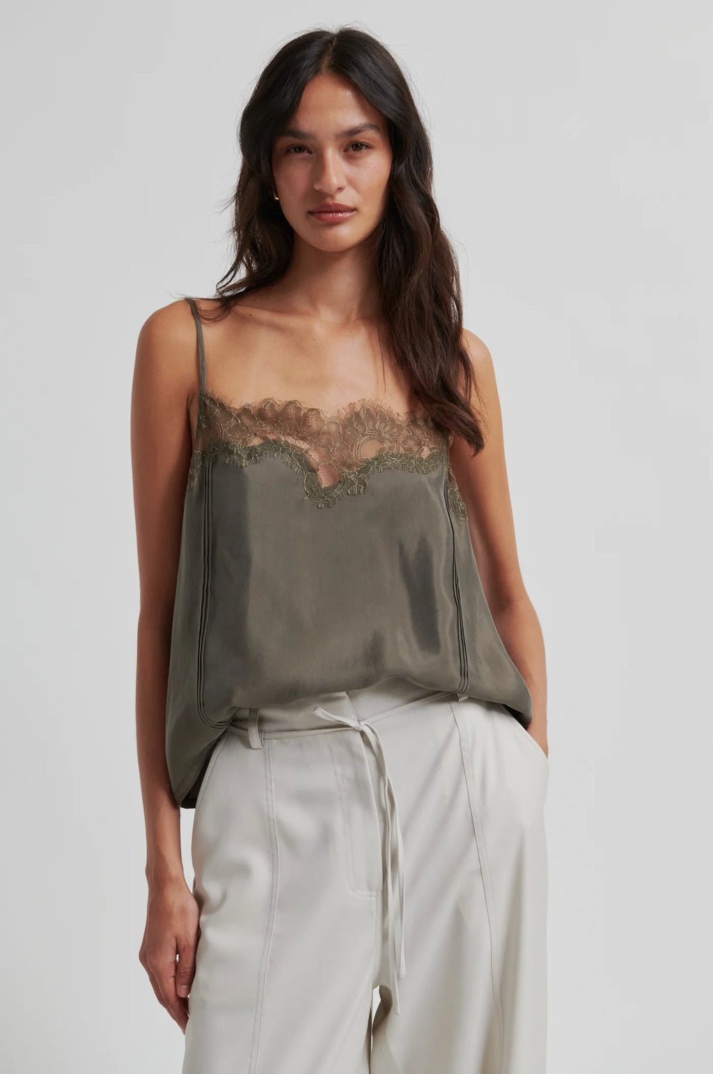 Woman wearing a green lace-trimmed top and light pants on a plain background
