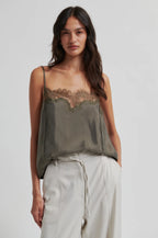 Woman wearing a green lace-trimmed top and light pants on a plain background