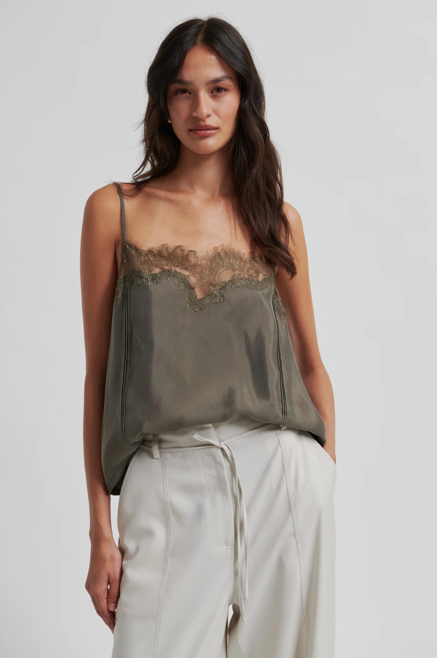 Woman wearing a green lace-trimmed top and light pants on a plain background