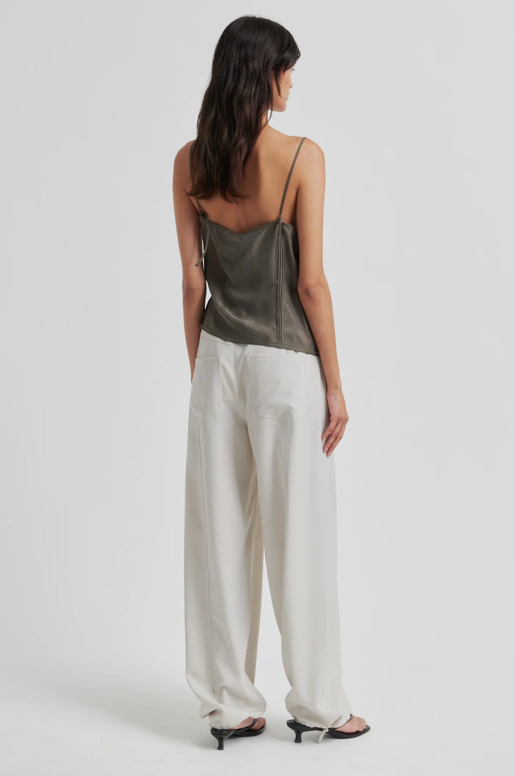 Woman wearing a green satin top and white pants on a white background