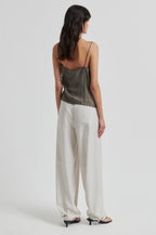 Woman wearing a green satin top and white pants on a white background