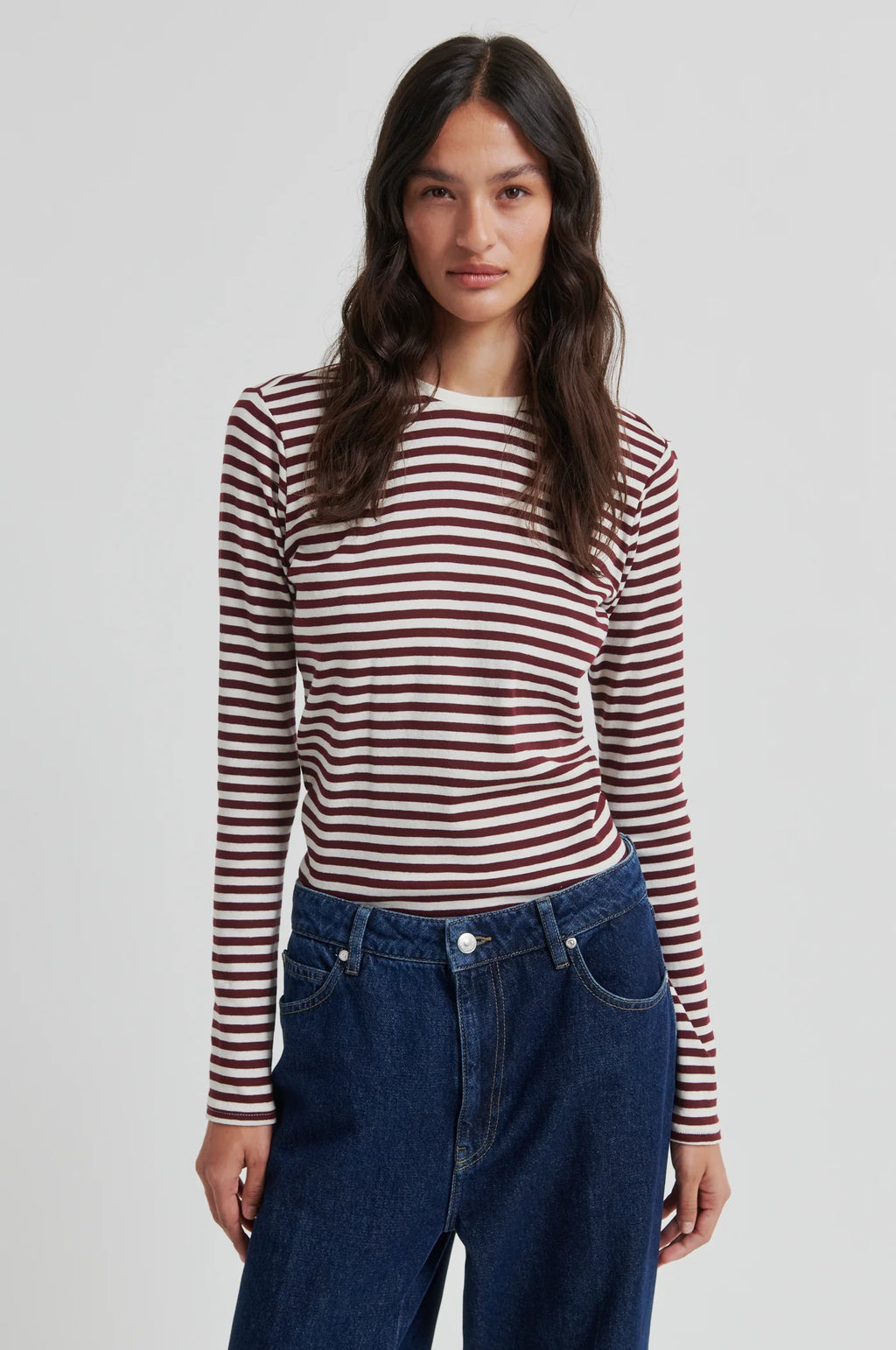 Woman wearing a striped long-sleeve shirt and blue jeans on a plain background