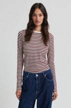 Woman wearing a striped long-sleeve shirt and blue jeans on a plain background