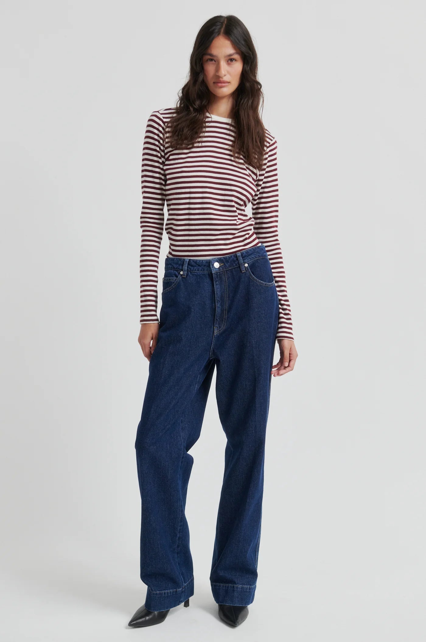 Woman wearing a striped shirt and blue jeans on a white background