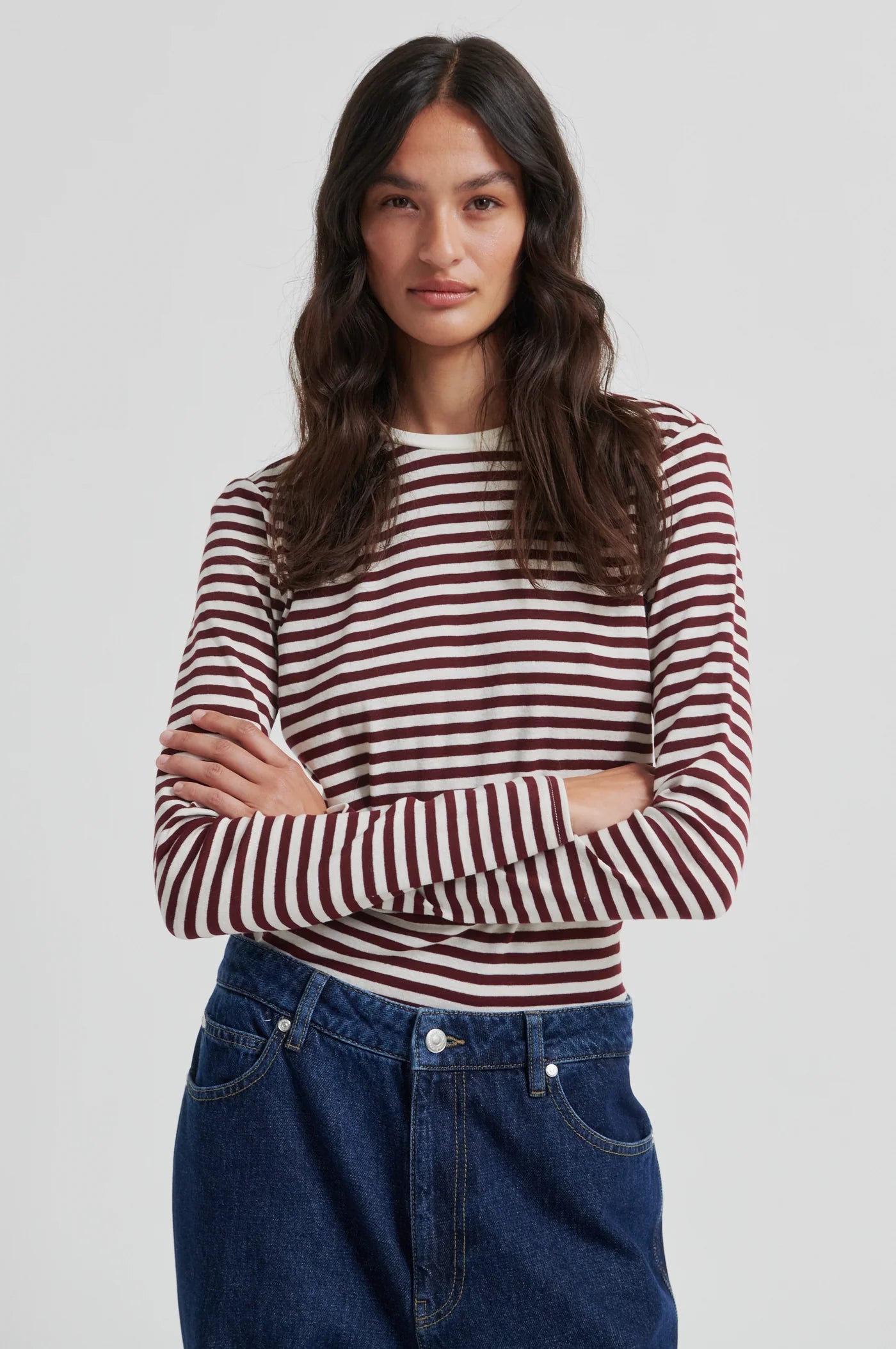 Woman wearing a striped shirt and jeans on a plain background