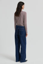 A woman is shown from the back wearing a long-sleeve striped knit top with dark blue wide-leg jeans against a light gray studio background.