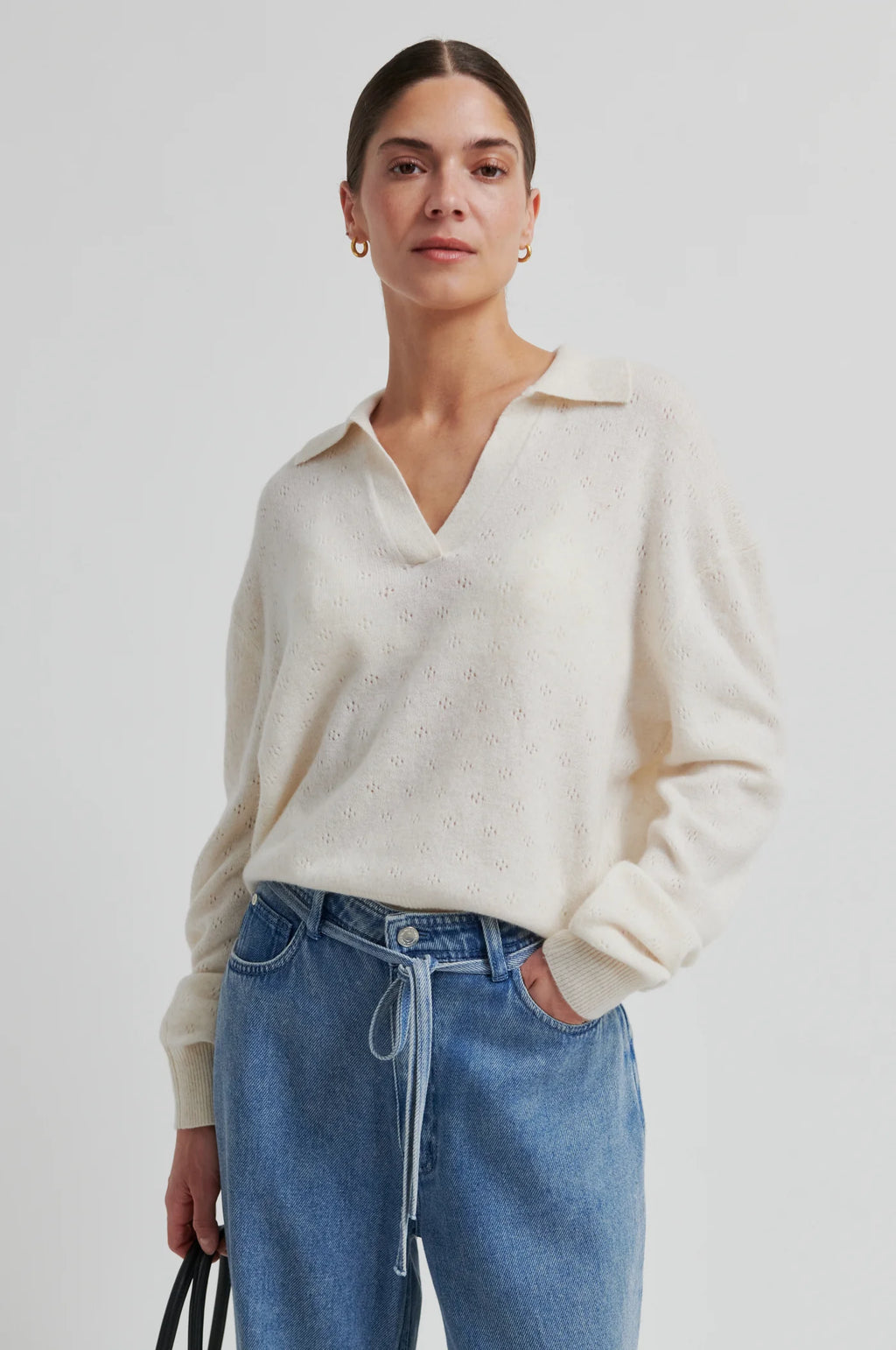 Woman wearing a cream sweater and blue jeans against a white background