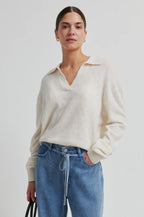 Woman wearing a cream sweater and blue jeans against a white background