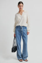 Woman wearing a white sweater and blue jeans holding a black handbag on a white background