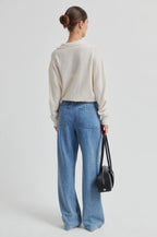 Person wearing a beige sweater and blue jeans holding a black bag on a light gray background