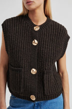 Black knitted vest with gold buttons worn by a person on a light gray background