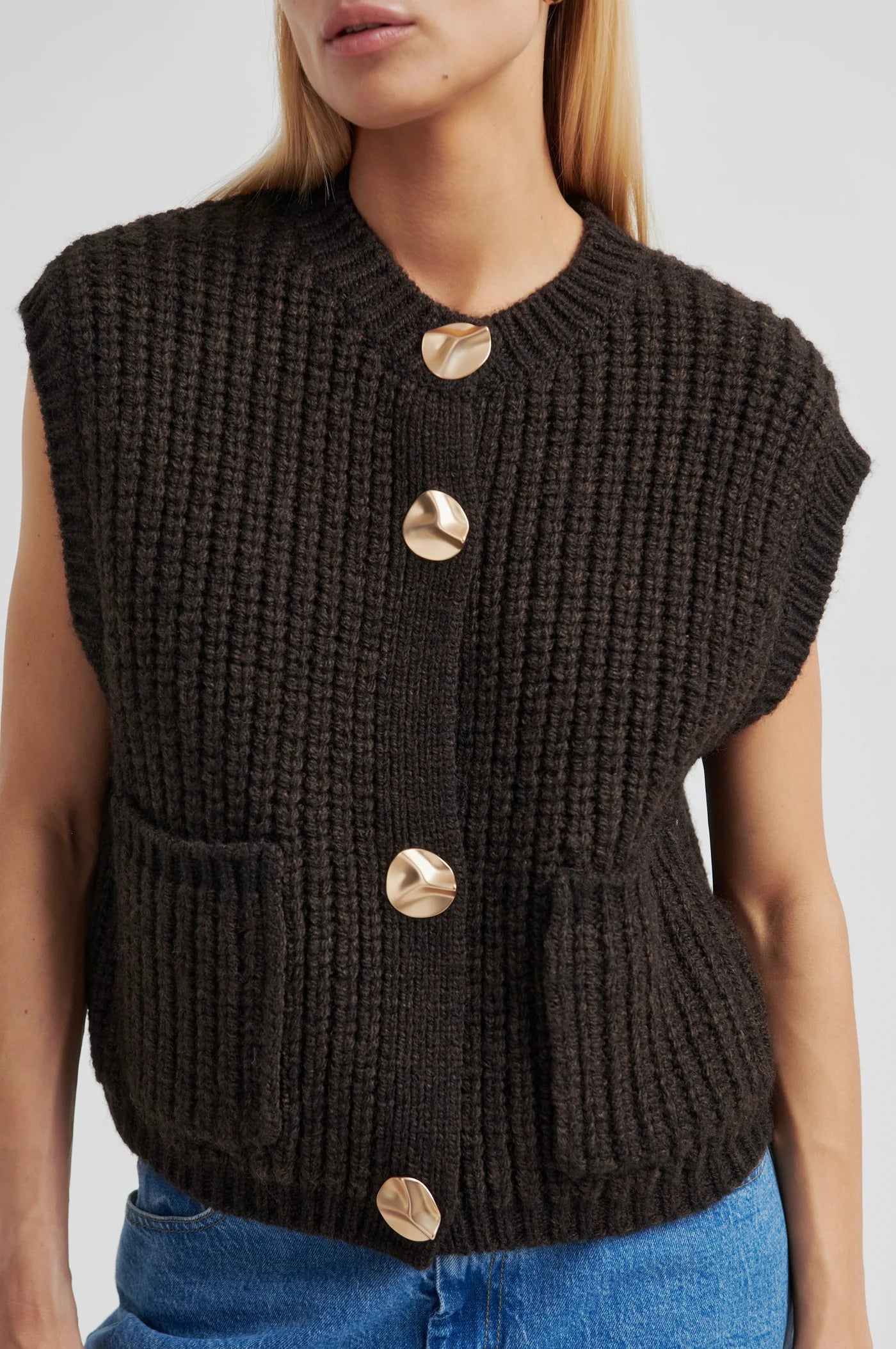 Black knitted vest with gold buttons worn by a person on a light gray background