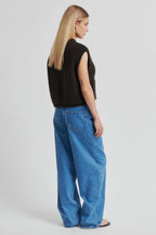 Person wearing a black sleeveless sweater and blue jeans on a white background