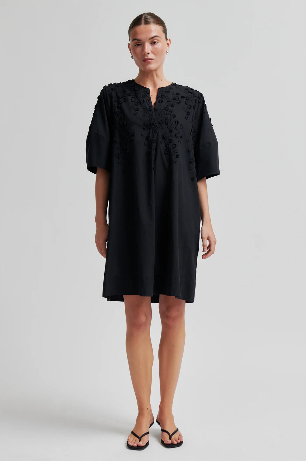 Woman wearing a black dress with floral embroidery on a white background