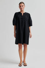 Woman wearing a black dress with floral embroidery on a white background