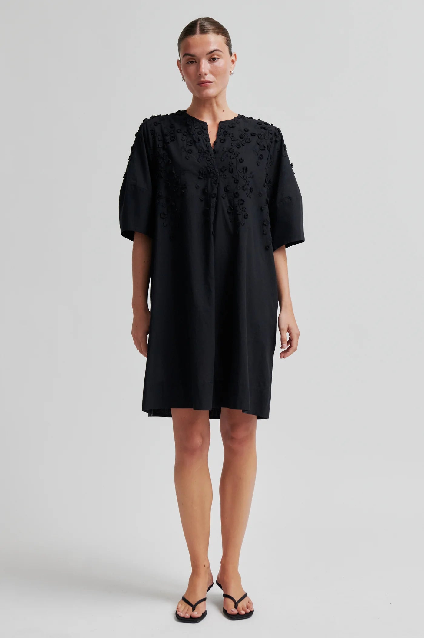 Woman wearing a black dress with floral embroidery on a white background