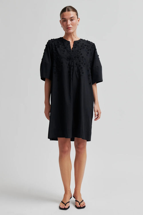 Woman wearing a black dress with floral embroidery on a white background