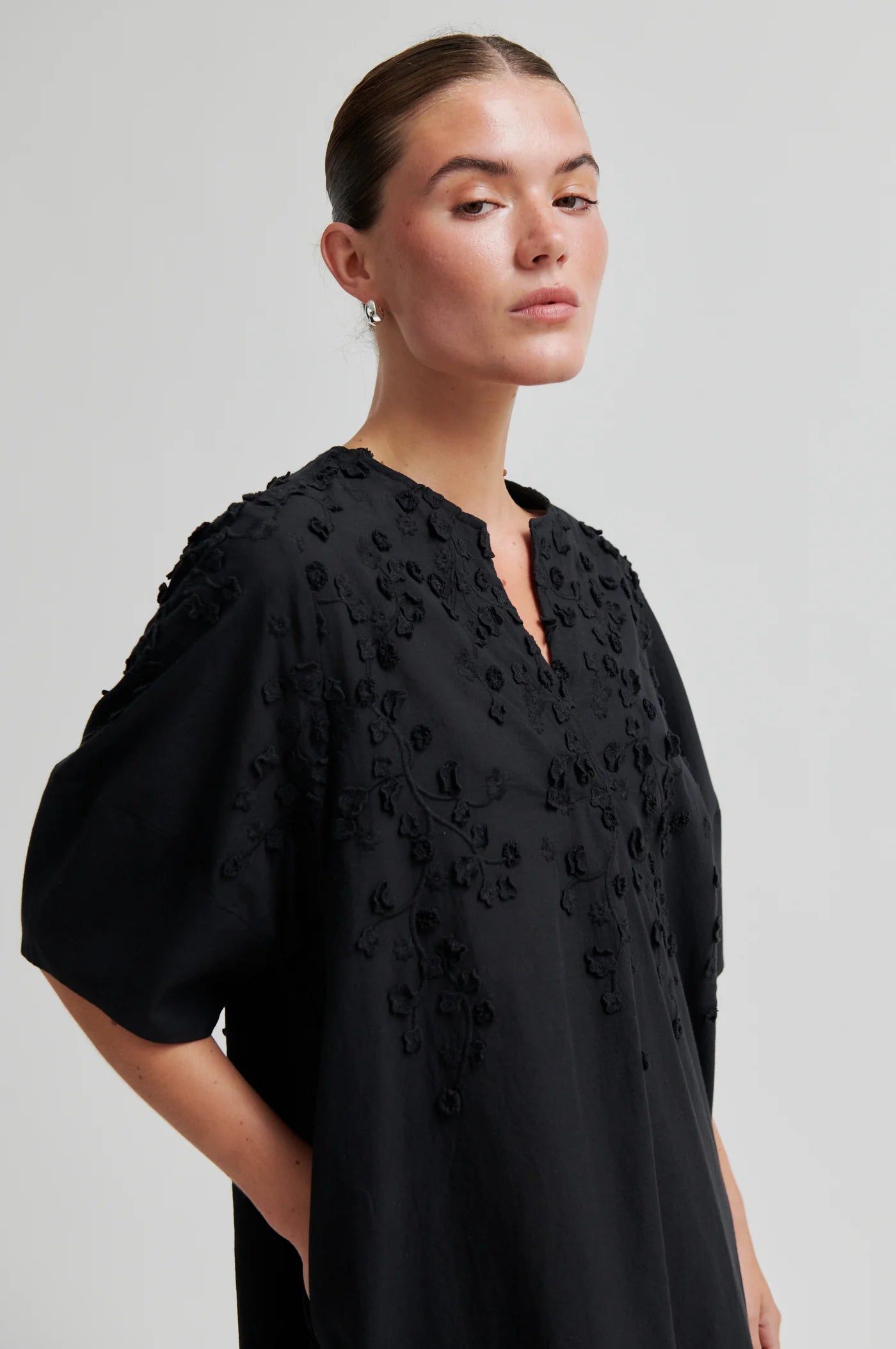 Woman wearing a black dress with floral embroidery on a light gray background