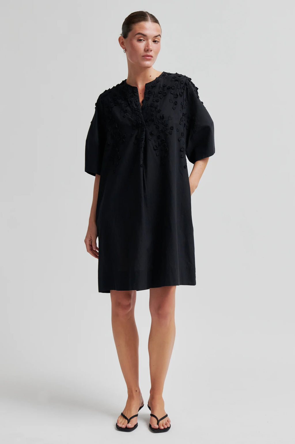 Woman wearing a black dress with floral embellishments on a plain background