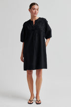 Woman wearing a black dress with floral embellishments on a plain background