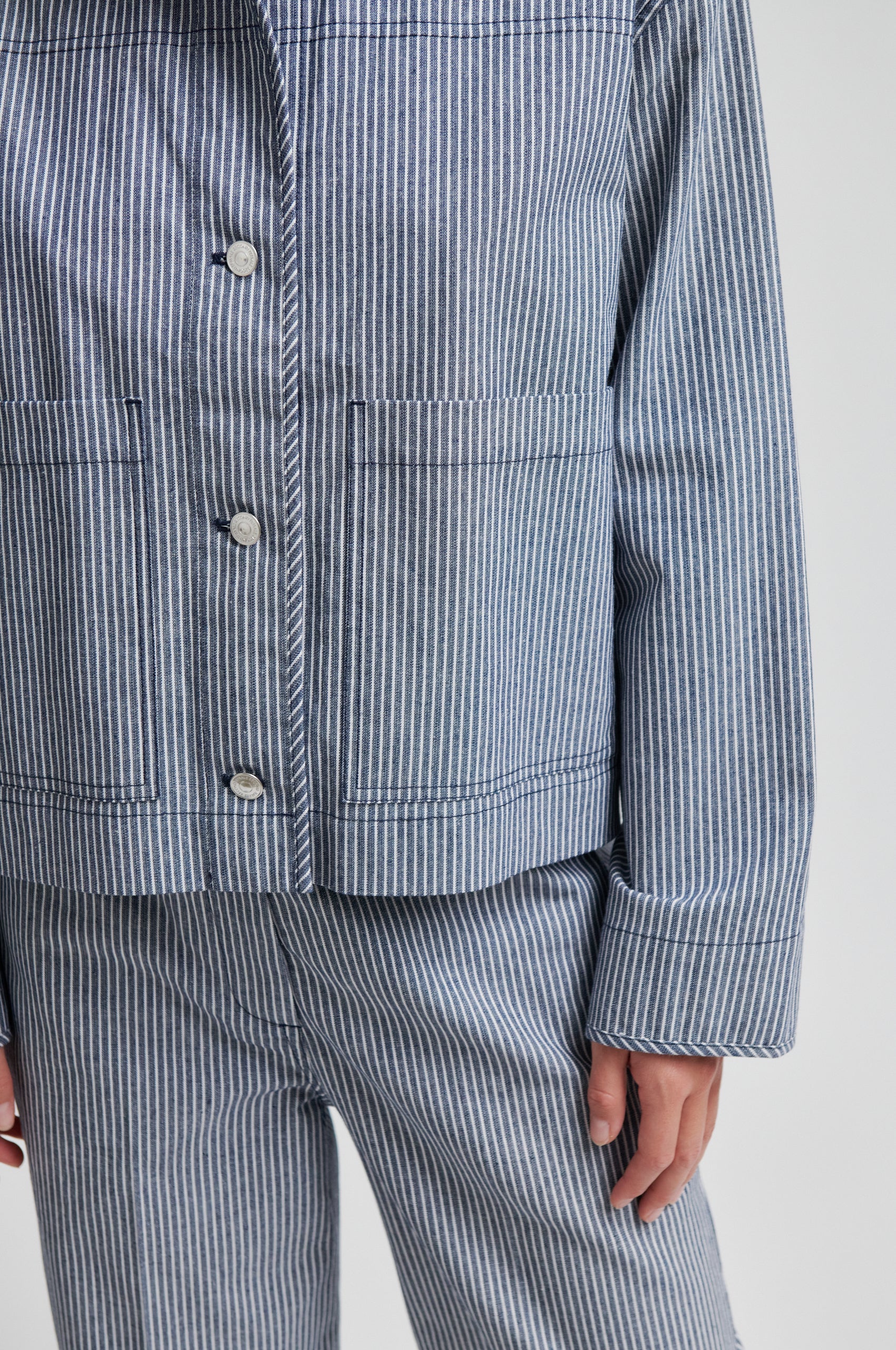 Close-up of a person wearing a blue and white striped shirt and pants on a light gray background