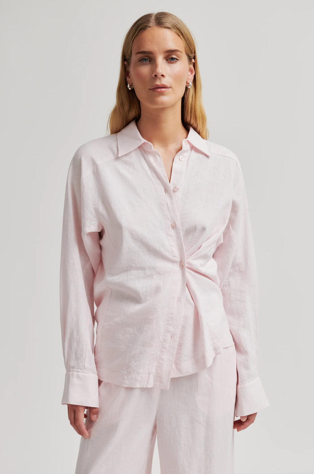 Woman wearing a light pink shirt and pants on a plain background