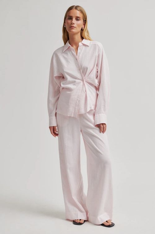 Woman wearing a light pink shirt and pants set on a white background