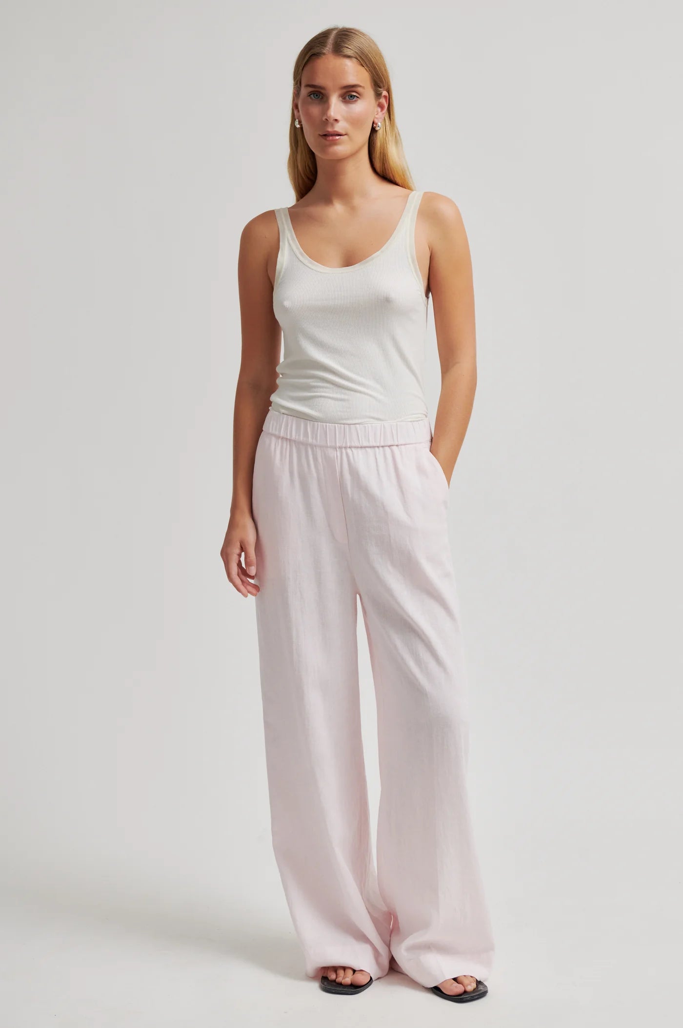 Woman wearing a white tank top and light pink pants on a white background