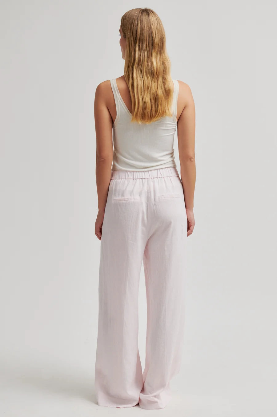 Woman wearing a white tank top and light pink pants on a plain background
