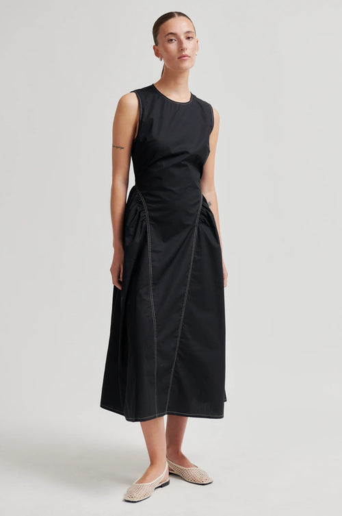 Woman wearing a black sleeveless dress on a plain background