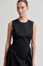 Woman wearing a black sleeveless dress against a plain background