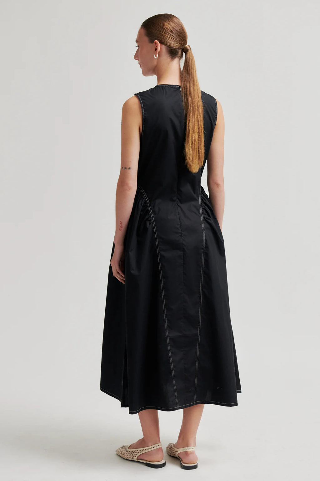 Woman wearing a black sleeveless dress on a plain background