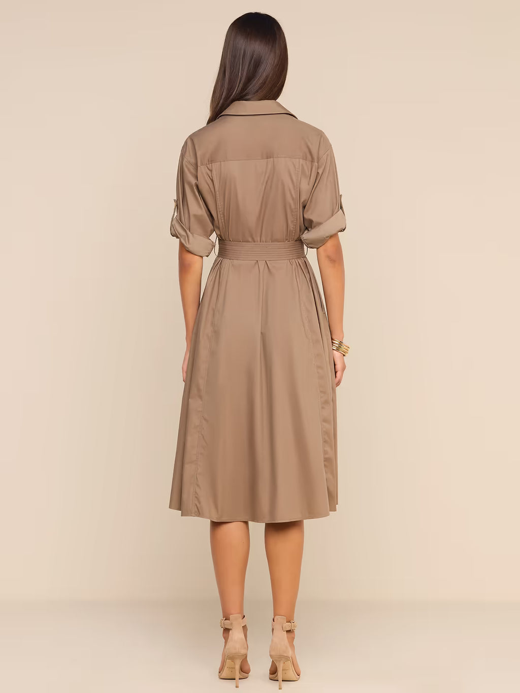 A woman viewed from the back wearing a taupe-brown short-sleeve collared dress with a matching waist belt, standing against a plain beige studio background.