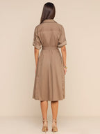A woman viewed from the back wearing a taupe-brown short-sleeve collared dress with a matching waist belt, standing against a plain beige studio background.