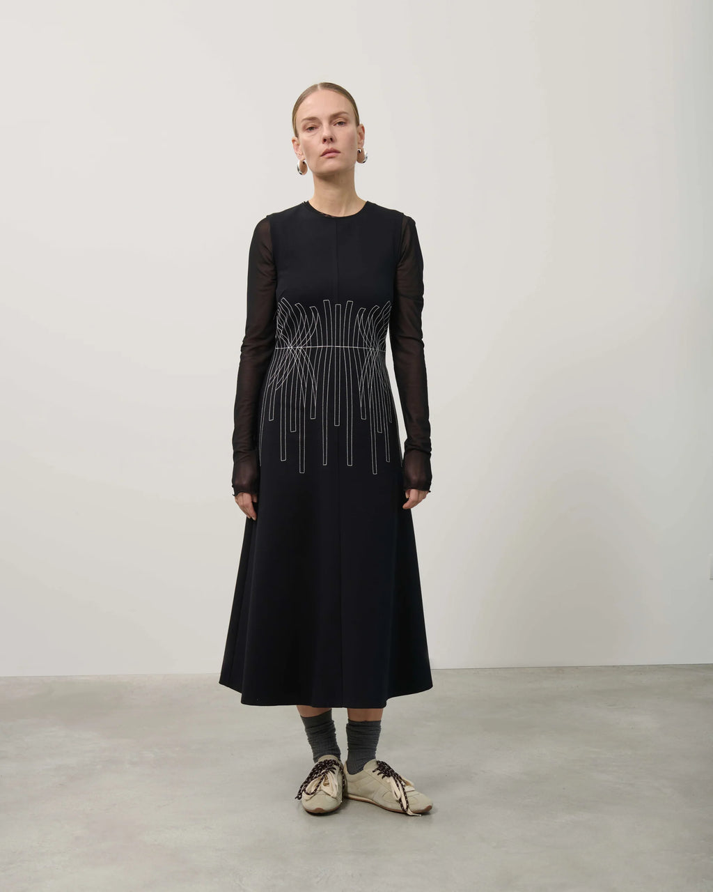 Person wearing a black dress with sheer sleeves and a white pattern on a plain background