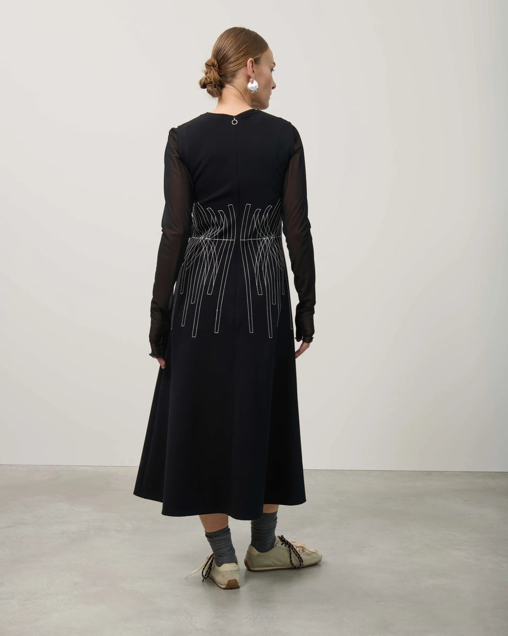 Woman wearing a black dress with sheer sleeves and geometric pattern on a plain background