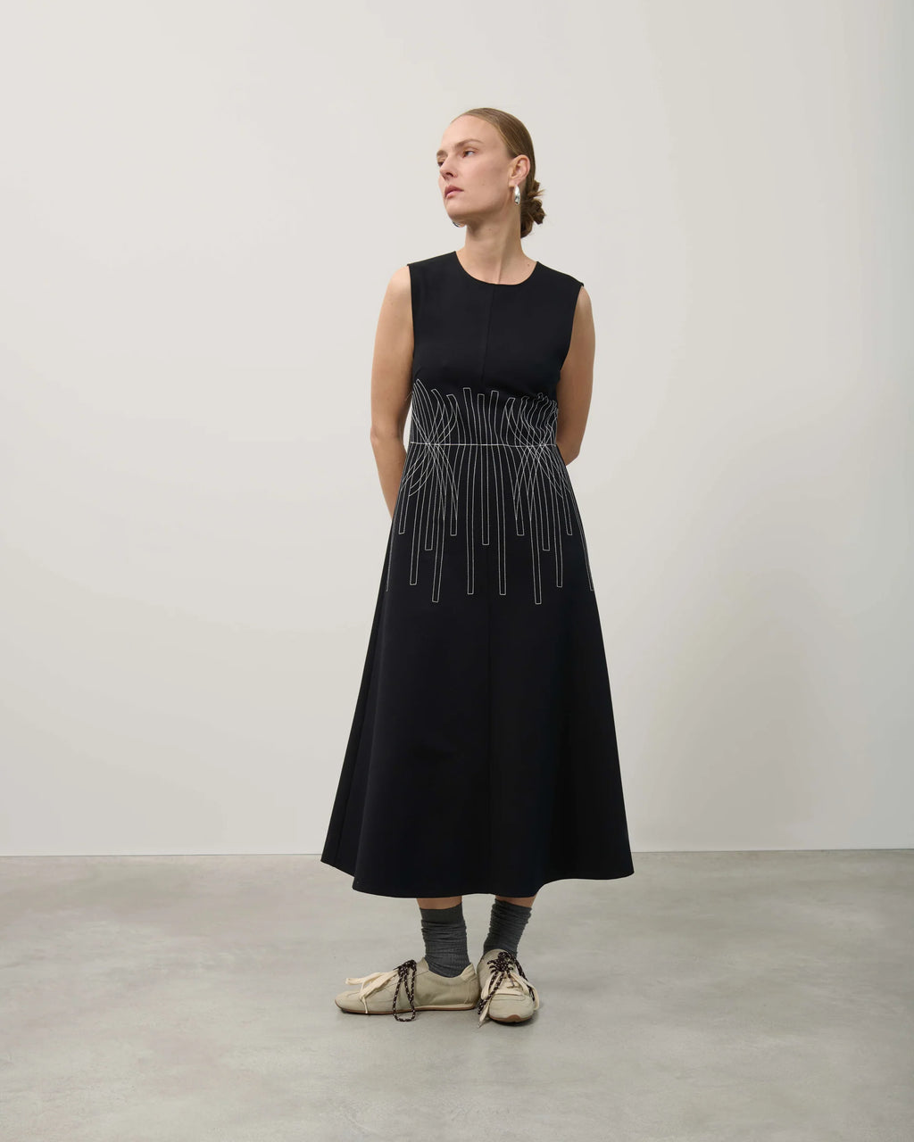 Woman wearing a black sleeveless dress with a beaded waistband against a plain background