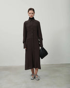 Woman wearing a brown outfit with a black bag on a plain background
