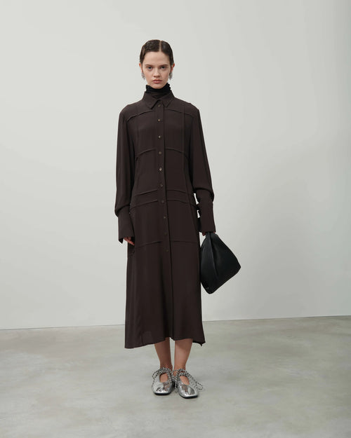 Woman wearing a brown outfit with a black bag on a plain background