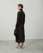 Woman wearing a dark brown coat holding a black bag against a plain background