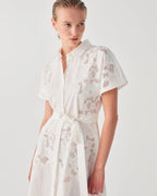 Woman wearing a white dress with cut-out patterns on a plain background