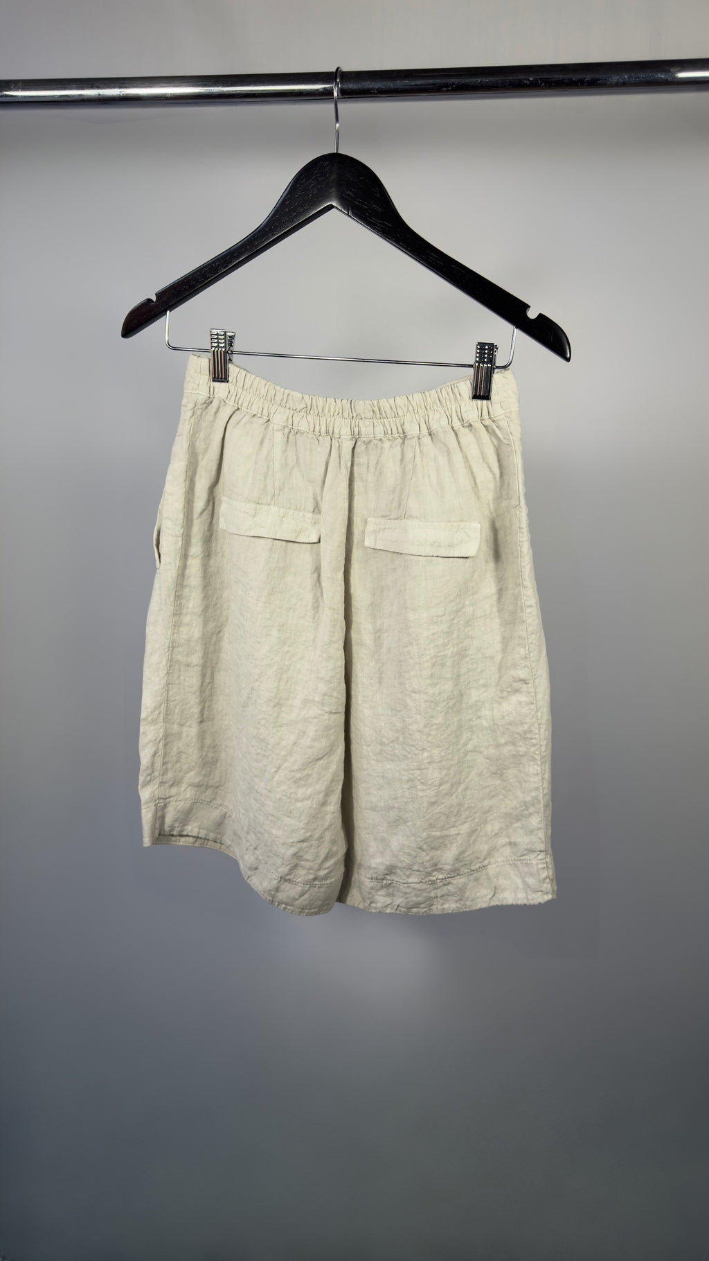 Beige shorts hanging on a black hanger against a gray background