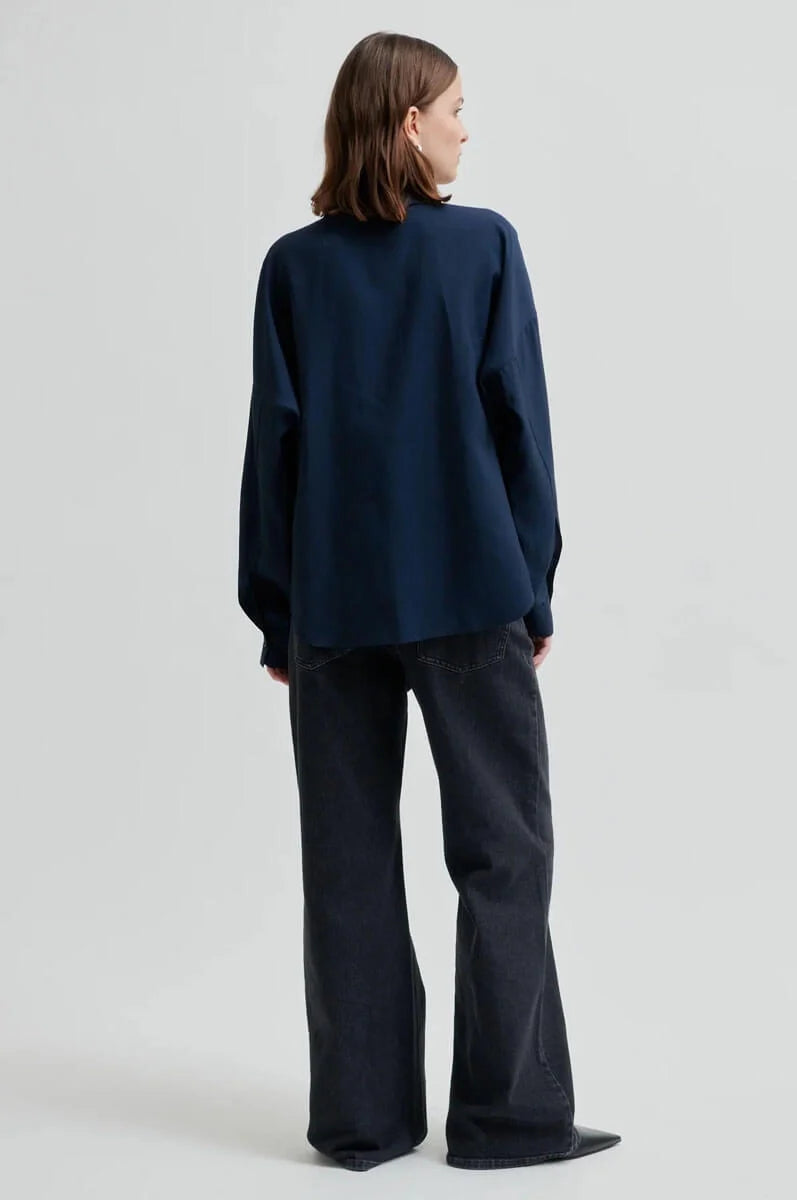 A model shown from the back wearing a dark navy blue long-sleeve top and dark wide-leg pants against a light gray studio background.