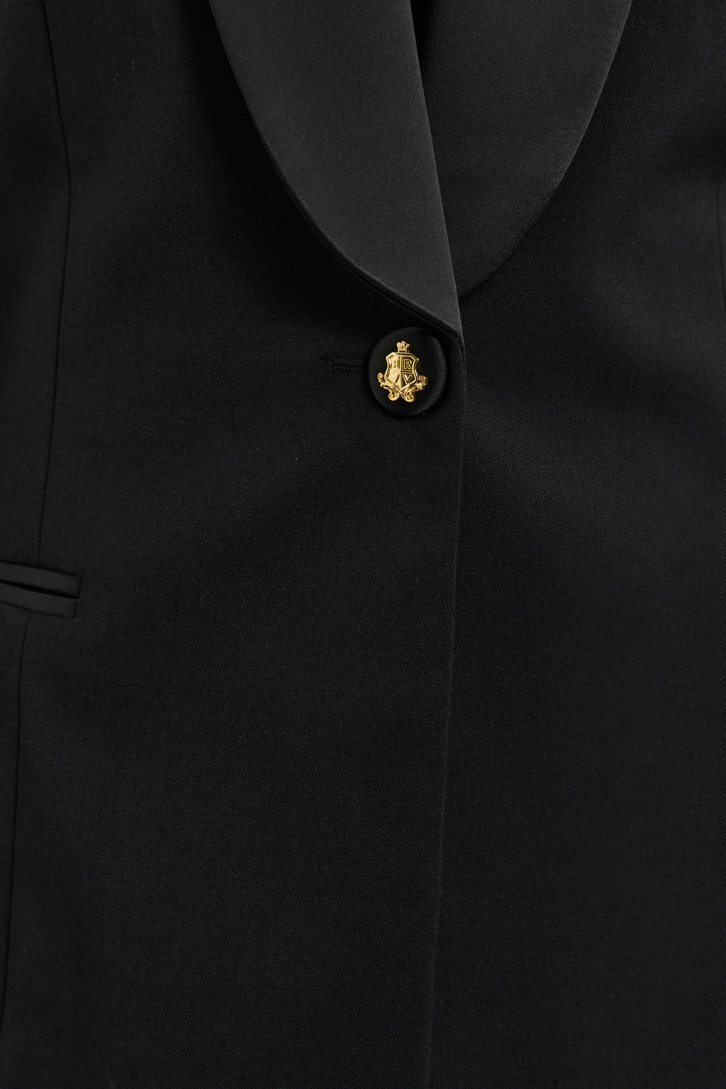 Close-up of a black suit jacket with a gold button on a black background