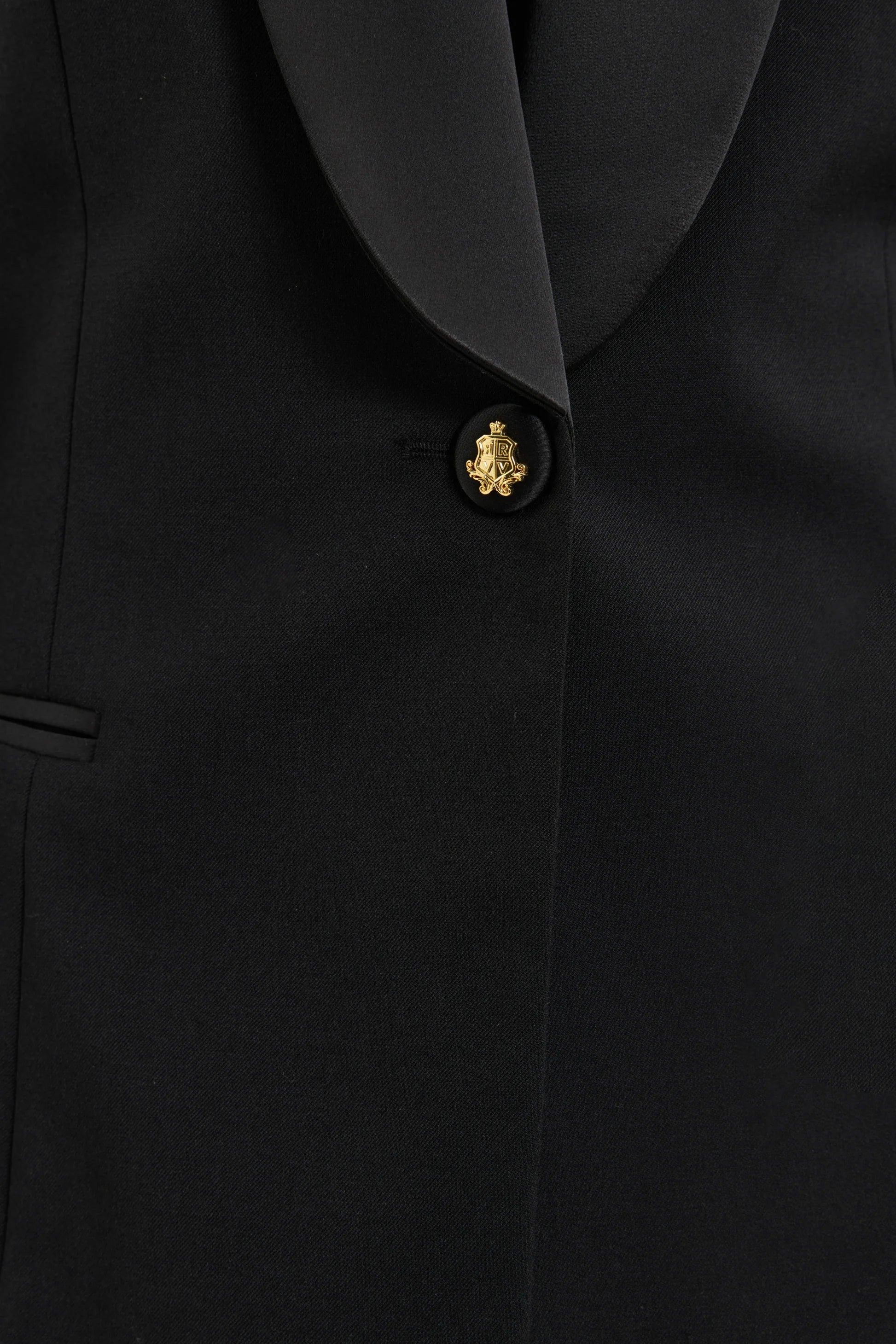 Close-up of a black suit jacket with a gold button on a black background