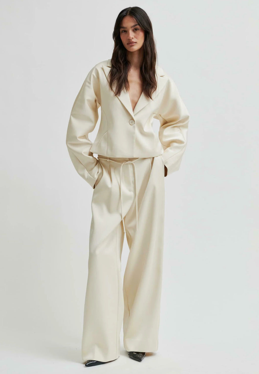 Woman wearing a cream satin suit against a white background