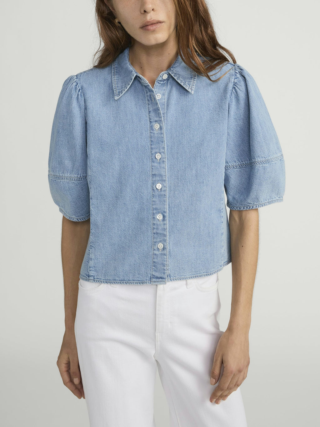 Woman wearing a light blue denim shirt with puff sleeves on a plain background