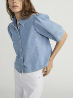 Woman wearing a light blue denim shirt and white pants on a plain background