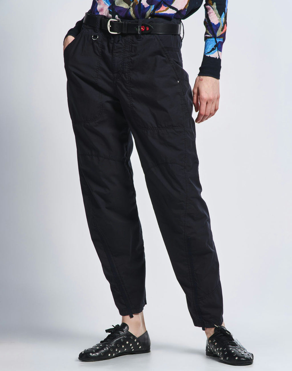 Person wearing black cargo pants with a colorful top and black shoes on a light gray background